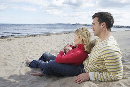 快乐的情侣在沙沙海滩上放松的侧面景象 看着海洋风景图片