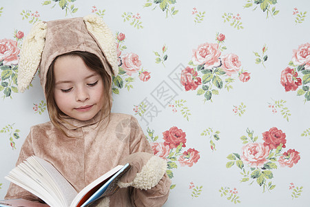 穿着兔子装扮的年轻女孩阅读书 与花粉型壁纸对立图片