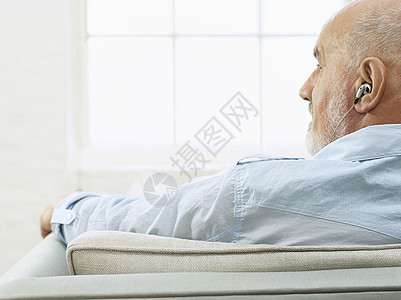 一个在沙发上戴耳机的成熟男子的近身后方视线 望着侧面背景图片