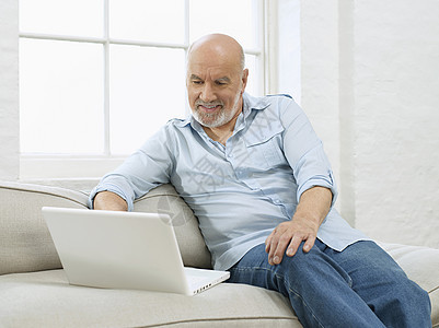 在家沙发上使用笔记本电脑的微笑成熟男子图片
