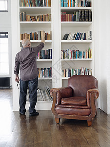 成年男子从书架上取书的全长后方视图成人退休地面房子房间学习硬木扶手椅搜索屏幕图片
