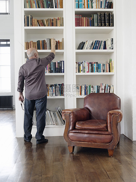 成年男子从书架上取书的全长后方视图成人退休地面房子房间学习硬木扶手椅搜索屏幕图片