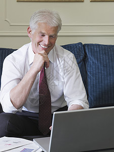 在沙发上使用笔记本电脑微笑的中年商务人士图片