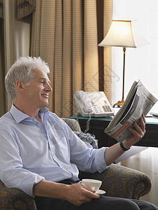 一个笑笑的中年商务人士坐在扶手椅上边看报纸的侧面景象图片