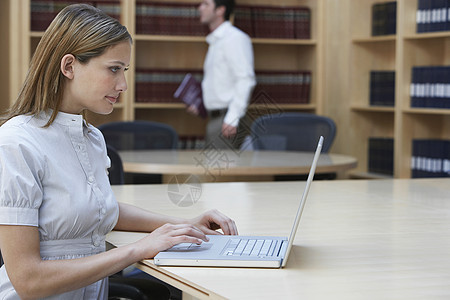 在法律办公室使用笔记本电脑的女性办公室工作者的侧面视图同事成人技术人士架子椅子桌面正装职业管理人员图片