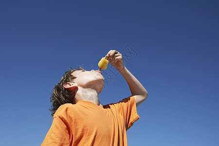 低角度观察一个小男孩 在清蓝的天空中吃冰棒背景图片