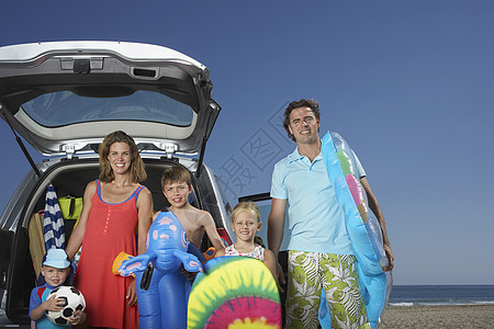 一对微笑的一对夫妇和三个孩子在海滩上乘车相撞的肖像图片