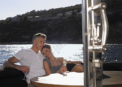 在游艇上坐桌边喝香槟的浪漫情侣图片