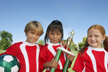 儿童足球队在战场上拿球和奖杯的肖像图片