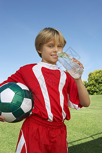 年轻足球运动员的肖像 他拿着球喝着饮用水图片