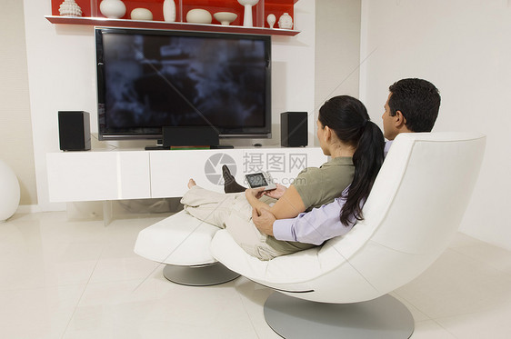 在看电视时坐在现代椅子上坐着一对轻松的情侣图片