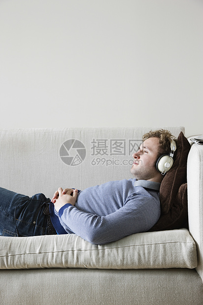 坐在客厅侧观的沙发上戴耳机的人休闲成人服装一人中年男人咖啡活动眼睛音乐图片