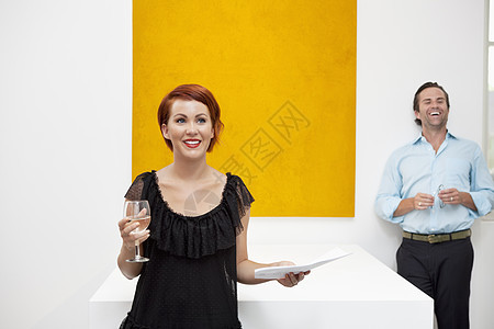 站在黄色画前的快乐女人 和背景男子一起站着图片