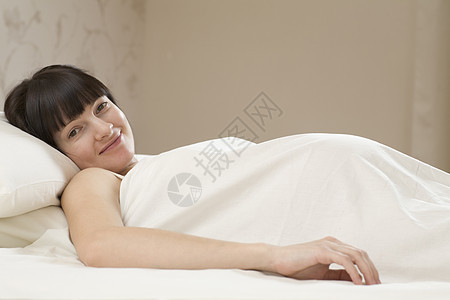 微笑着的年轻孕妇躺在床上的肖像图片