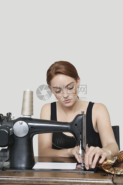 彩色背景下缝纫机上的年轻女裁缝缝纫布图片