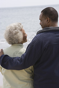 男人用手臂围着一个女人 在水边的边缘外套成人海滩女士羊毛夫妇年龄退休夫妻微笑图片