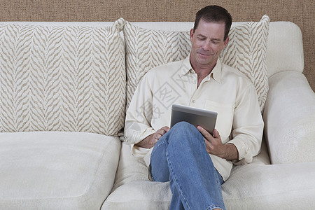 新媒体男人坐着看数字书双膝电子书生活微笑扶手椅阅读电子软垫成人牛仔裤背景
