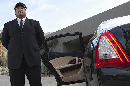 司机站在豪华车的敞开汽车门前一人帽子男人正装套装车门黑色尾灯奢华长度图片