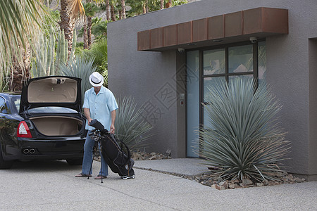 男子将高尔夫球袋提升到豪华车的靴子上图片