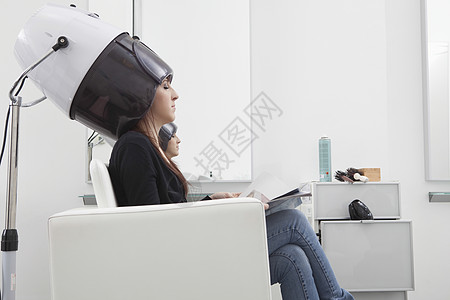 女客户在理发厅坐在干衣帽下图片