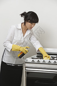 利用灰色背景的年轻女仆清洁炉灶图片