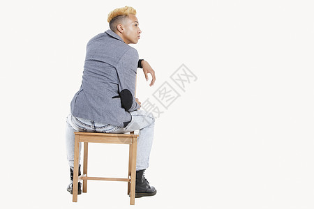 年轻男孩坐在椅子上时的背面景象 当他仰视灰色背景图片