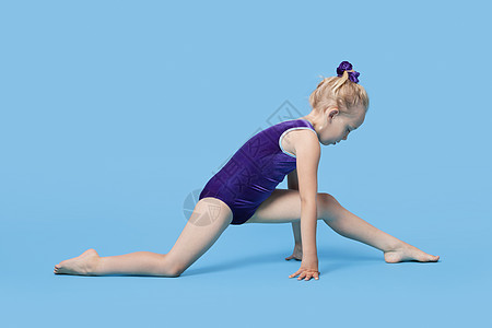 身穿体服的年轻女孩在蓝色背景上伸展腿部图片