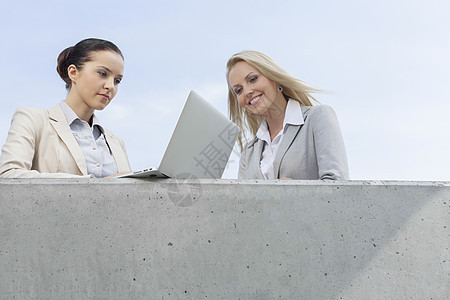 使用笔记本电脑与同事站在天对天的露台上时商业女商务人士的低角度视角图片