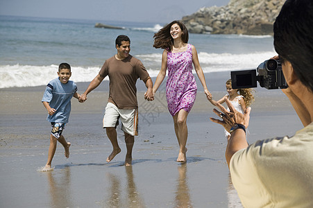 男子录像记录快乐的西班牙裔拉丁家庭在海滩散步图片