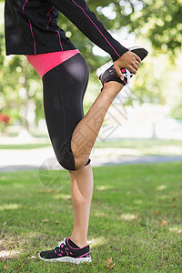 女性在公园锻炼时伸展腿的侧面视图图片