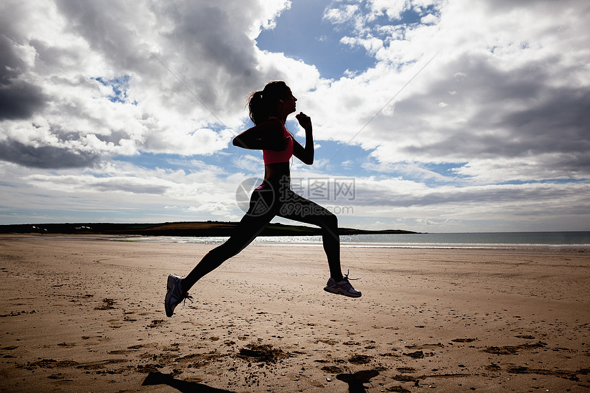 在海滩上慢跑的完整健康的女子长长的轮光影图片