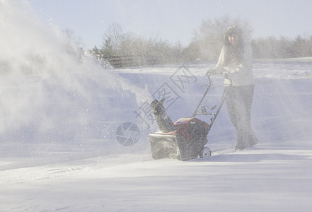年轻妇女与吹雪者清扫车投掷者季节冷冻车道降雪机器工作打扫女士鼓风机图片