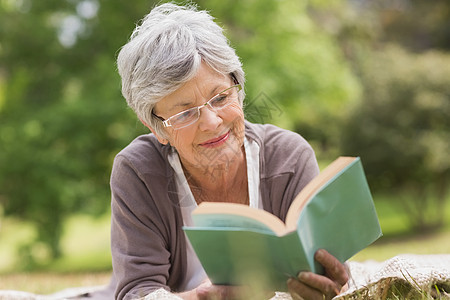 在公园看书的年长妇女树木闲暇专注成人地毯人员页数微笑女性阅读图片
