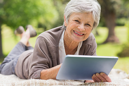 在公园使用数字平板牌的老年微笑妇女头发女士闲暇人员平板快乐电脑说谎灰色成人图片