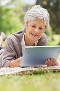在公园使用数字平板牌的老年微笑妇女头发退休闲暇女士药片农村成人说谎灰色触摸屏图片