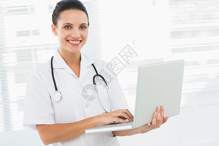 一名使用笔记本电脑微笑的女医生的肖像女士从业者医疗保健女性职场医务室服务办公室诊所工作服图片