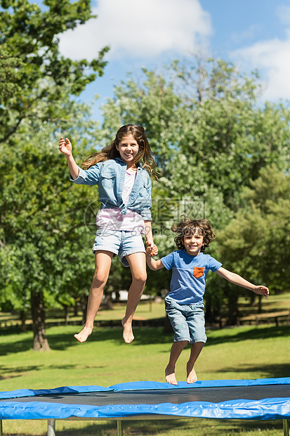 快乐的男孩女孩跳高在公园的蹦床上图片