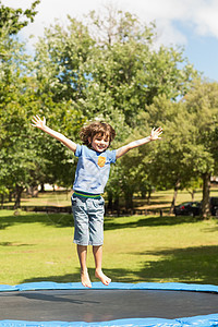 快乐男孩在公园的蹦床上跳高图片