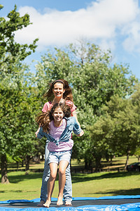 快乐的女孩和母亲在公园的蹦床上跳高空气家庭活动运动娱乐女儿闲暇享受妈妈飞行图片