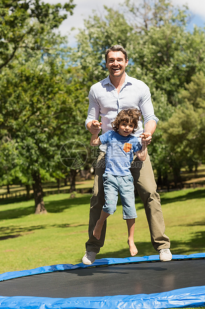 快乐的男孩和父亲在公园的蹦床上跳高图片