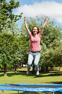 快乐的女人在公园的蹦床上跳高图片