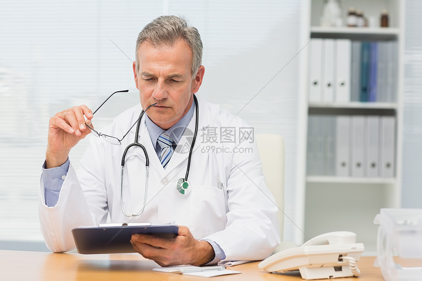 重点医生用剪贴板坐在办公桌旁图片
