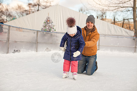 年幼父亲教他女儿滑溜冰在水晶上冰鞋学习手套溜冰者婴儿享受孩子教育童年溜冰场图片