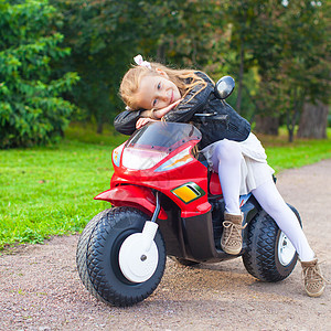 穿着皮夹克的可爱快乐的小姑娘 坐在玩具摩托车上引擎微笑自行车运输速度姐姐游戏喜悦乐趣娱乐图片