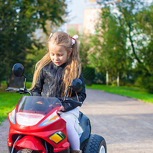 穿着皮夹克的小可爱摇滚女孩的肖像 坐在玩具摩托车上坐着乐趣自行车娱乐童年速度幼儿园晴天微笑运输喜悦图片