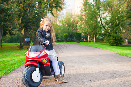 可爱的小可爱女孩 在绿公园骑自行车玩得开心孩子晴天游戏速度喜悦运动引擎乐趣姐姐玩具图片