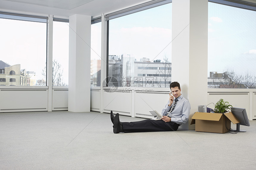 办公室工作人员在空办公空间的地板上用电话交谈;图片