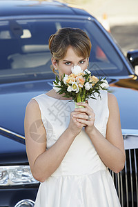 在豪华轿车肖像前拿着花束的年轻女子图片