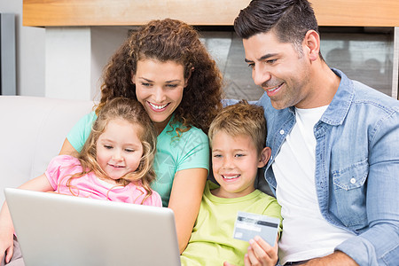 妈妈的微笑幸福的家庭坐在沙发上用笔记本电脑一起上网购物背景