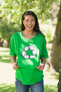 在公园中穿着绿色回收运动衫的微笑妇女快乐保护环境黑发展示生态活动家女性女士背景图片
